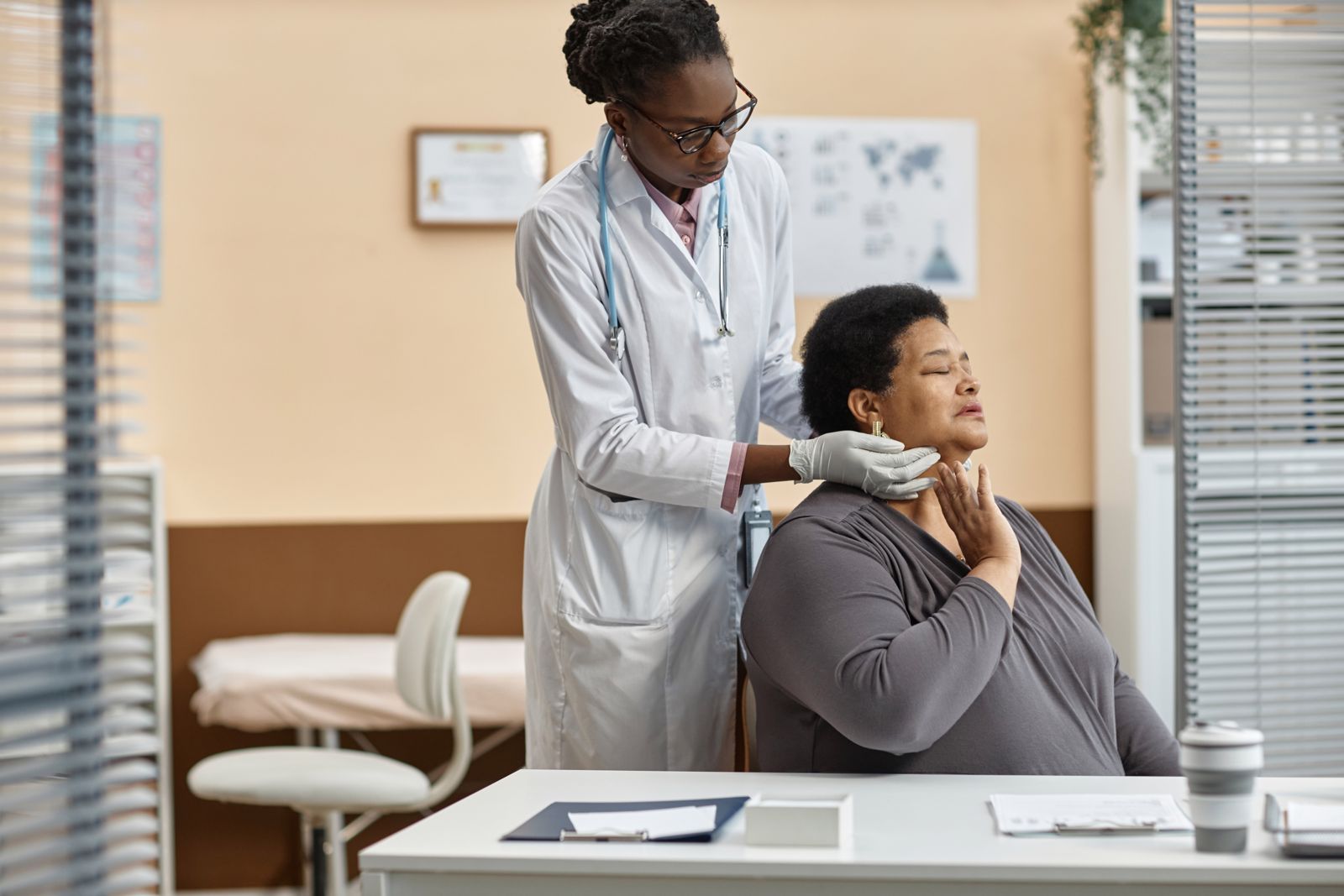 A physician examining a patient's neck in an exam room.