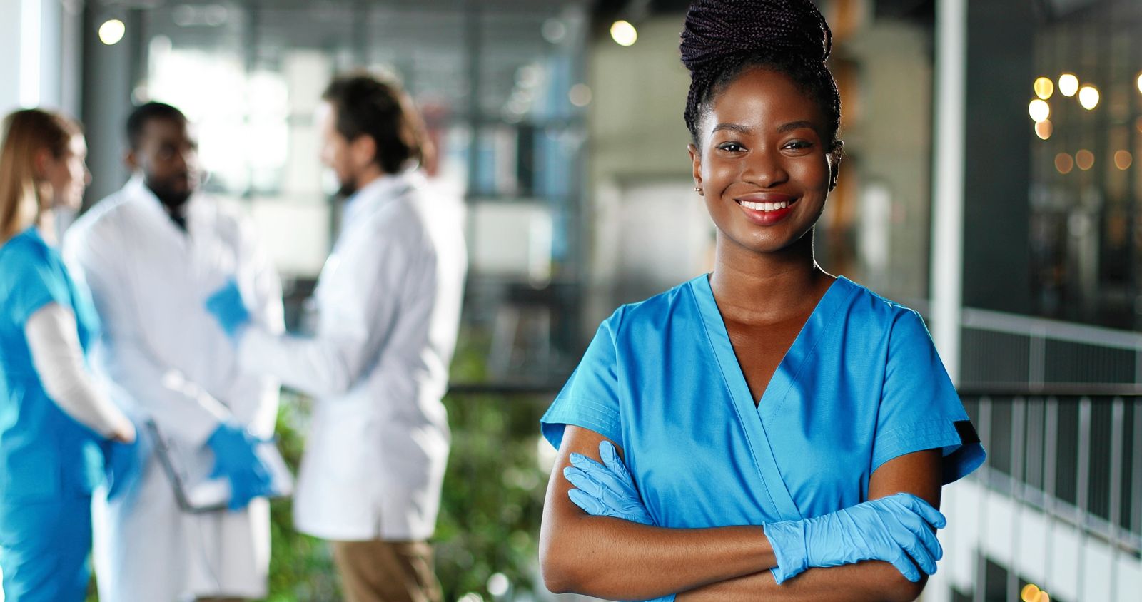 A smiling clinician in blue scrubs with colleagues behind her.